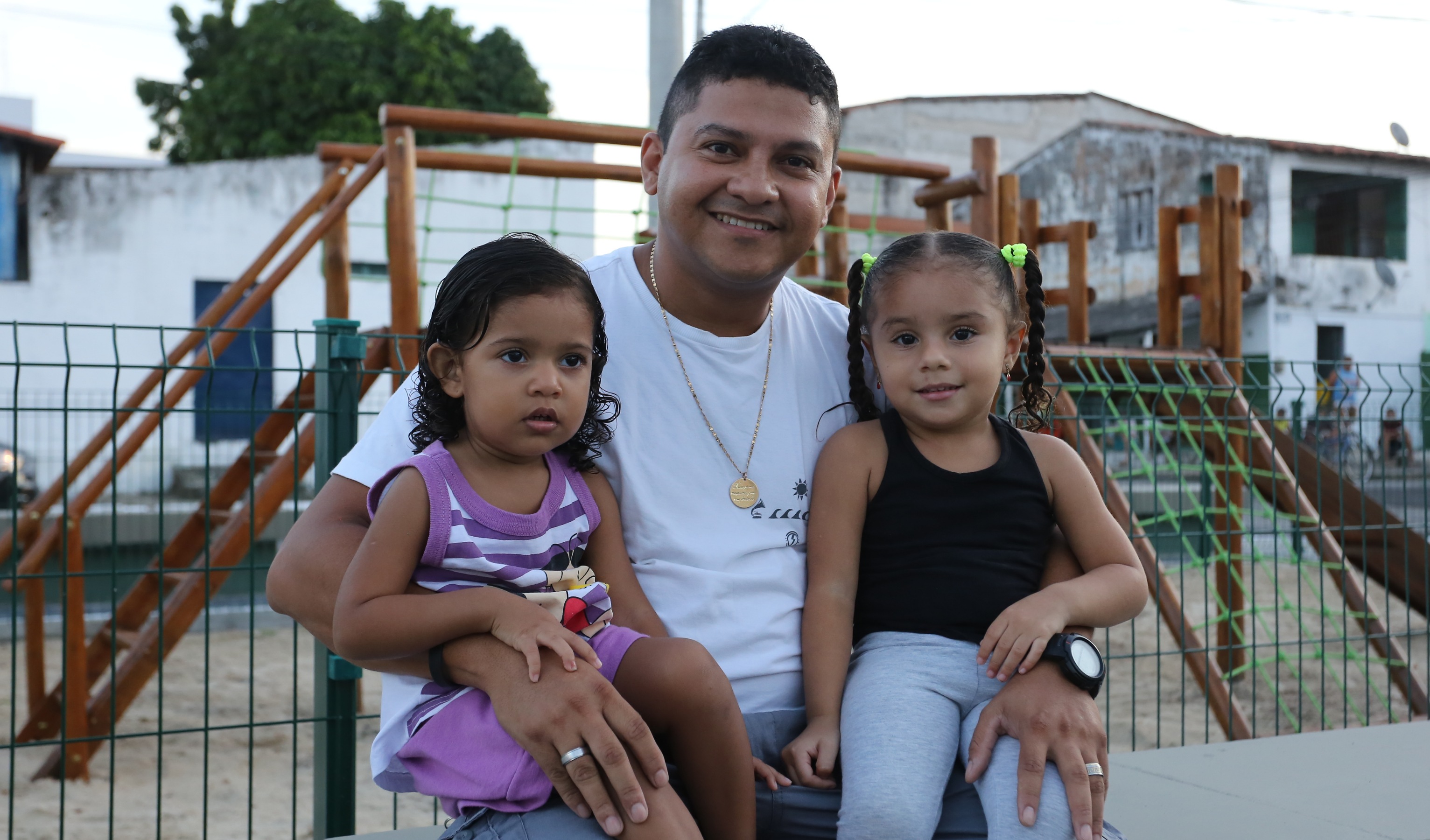 homem sorrindo para a foto abraçando duas meninas também sorrindo